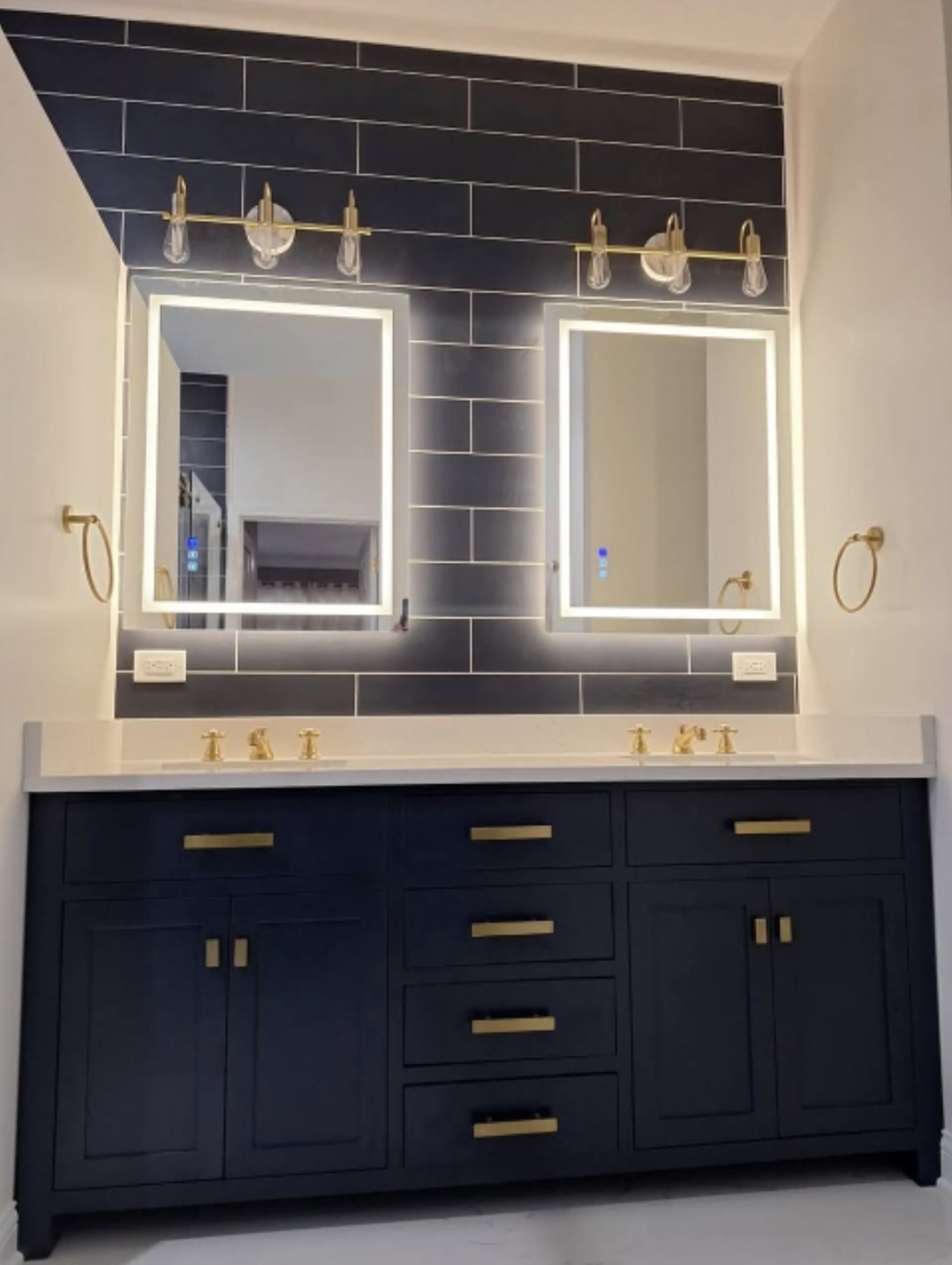 Bathroom with double vanity, backlit mirrors and black subway tile